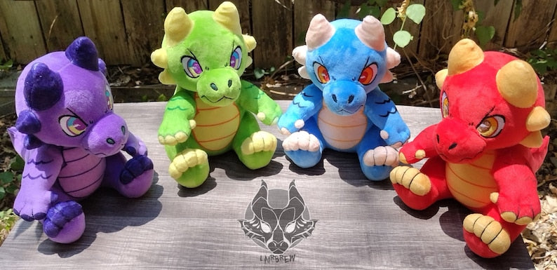 A purple kobold plush, green kobold plush, blue kobold plush, and red kobold plush sitting outdoors. They are all sitting on their own with no support. Each has an embroidered mischevious expression, 6 horns on their head, and a round tummy.
